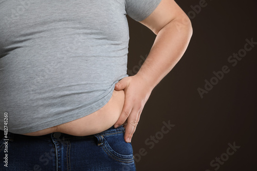 Overweight man in tight t-shirt on dark brown background, closeup. Space for text. © New Africa