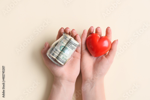 Female hands with red heart and jar with money on color background, closeup. Donation concept