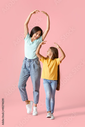 Happy dancing woman and her daughter on color background