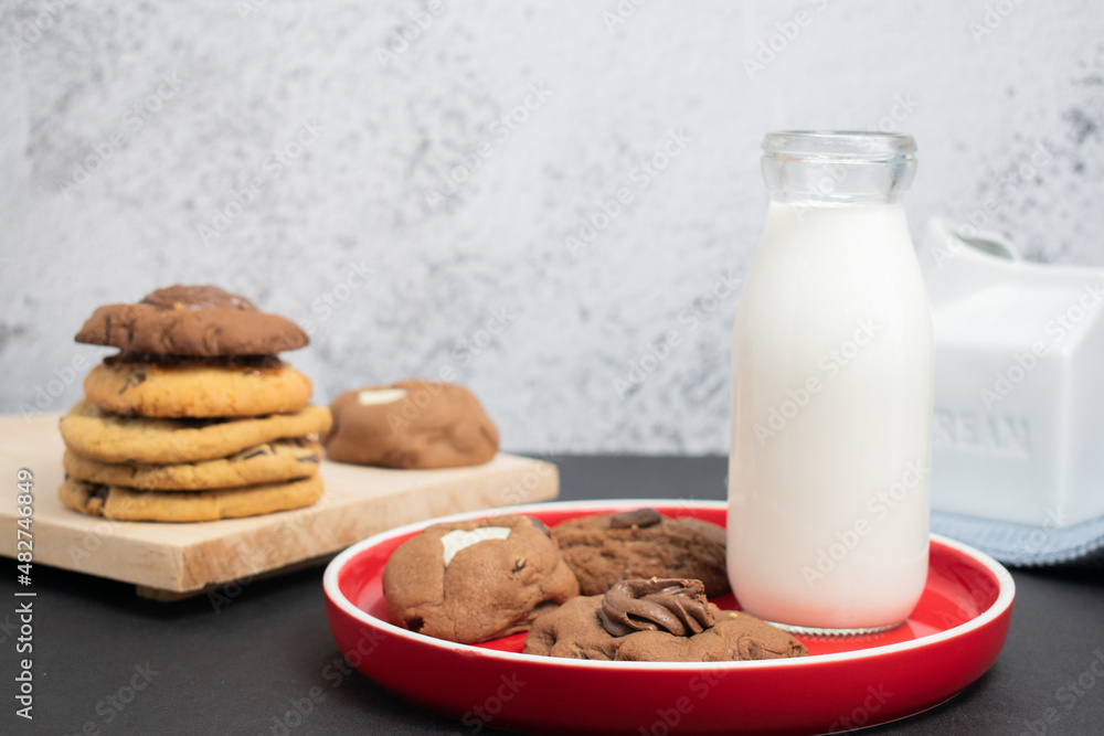 Galletas de chocolate con vaso de leche sobre plato rojo Galletas de chocolate con vaso de leche sobre plato rojo