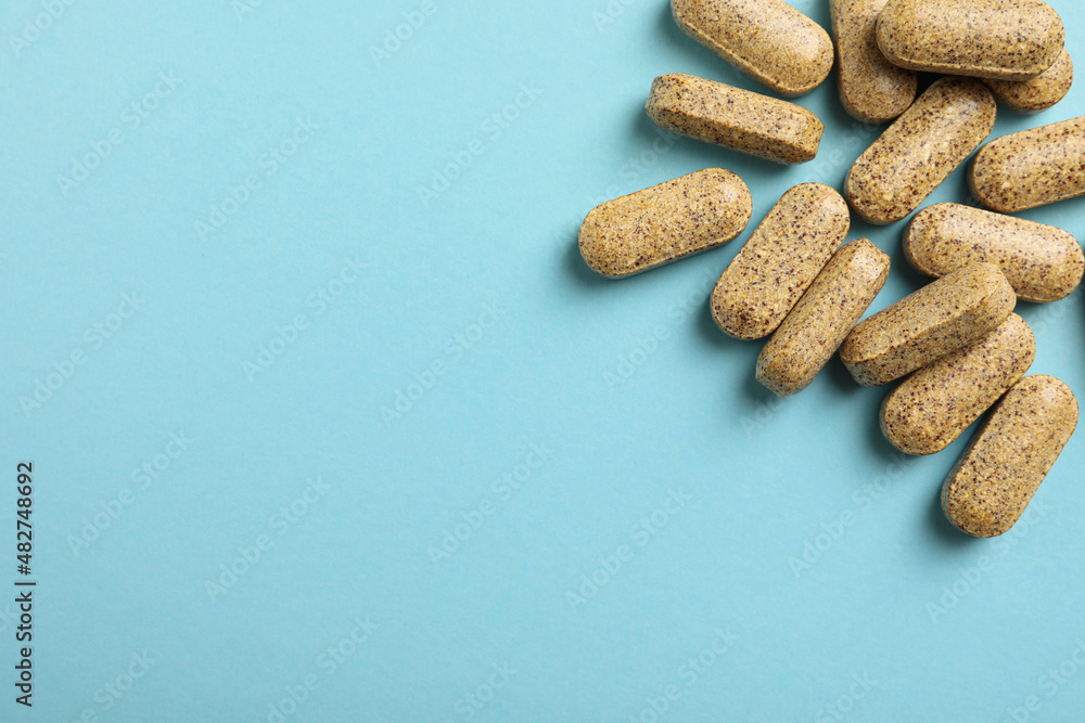 Dietary supplement pills on light blue background, flat lay. Space for text