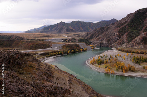 The bend of the picturesque turquoise river flowing at the foot of the high mountains through the autumn valley.