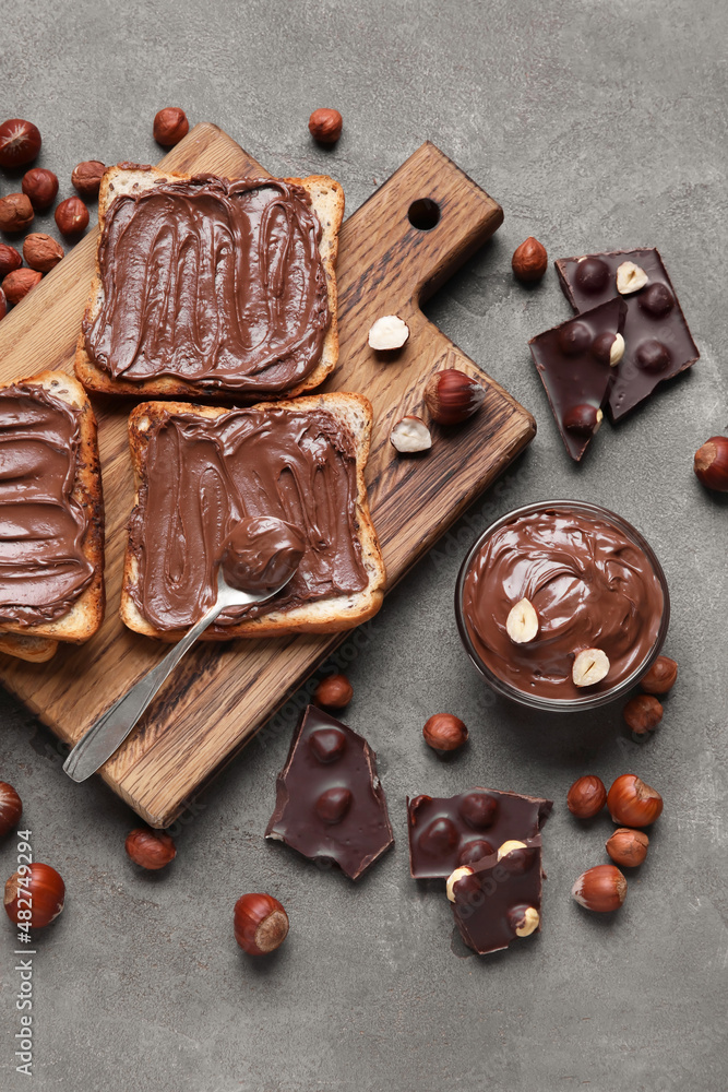 Wooden board of bread with chocolate paste and hazelnuts on grey background Wooden board of bread with chocolate paste and hazelnuts on grey background