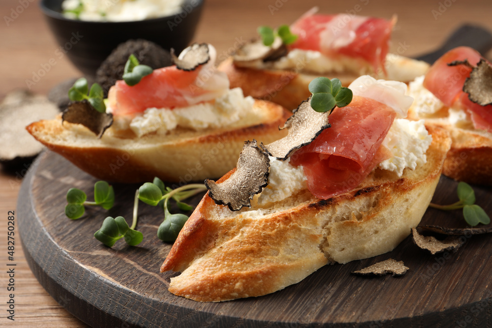 Delicious bruschettas with cheese, prosciutto and slices of black truffle on wooden table, closeup
