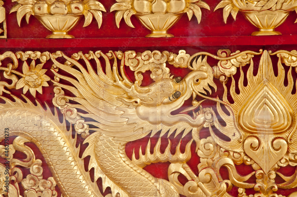 Golden majestic traditional Asian dragon sculpture on dark red wooden wall in temple