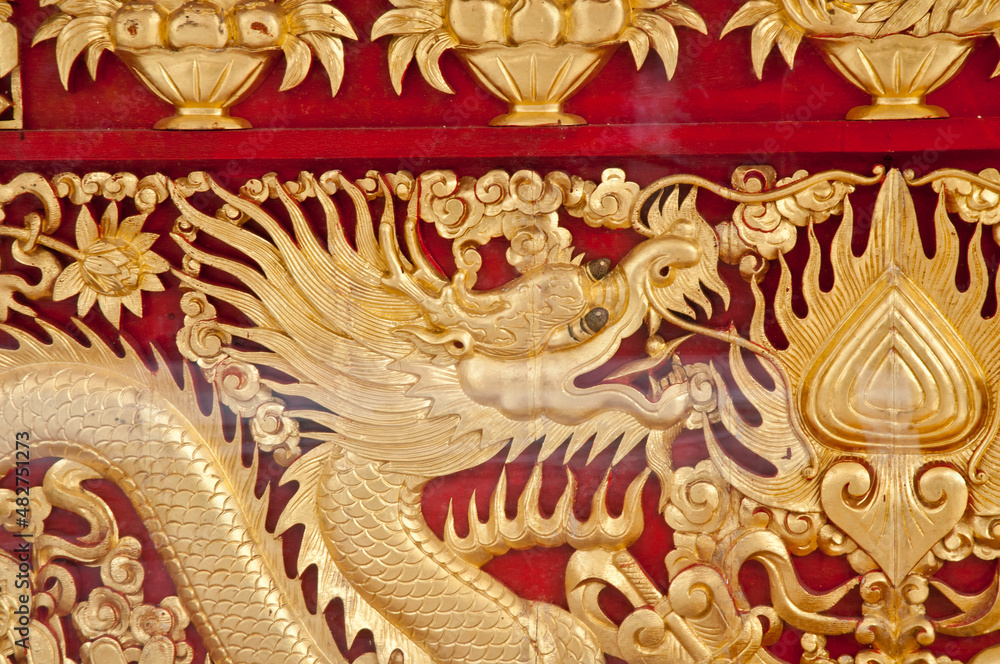 Golden majestic traditional Asian dragon sculpture on dark red wooden wall in temple Golden majestic traditional Asian dragon sculpture on dark red wooden wall in temple
