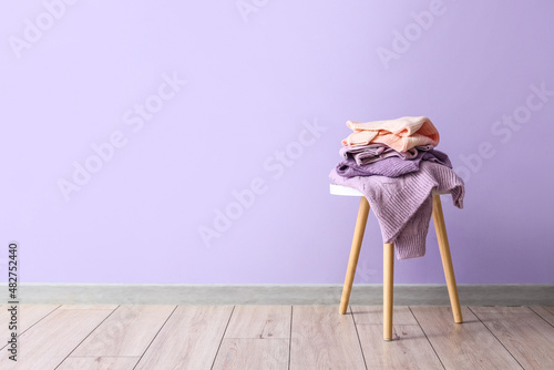 Stack of warm sweaters on table near lilac wall