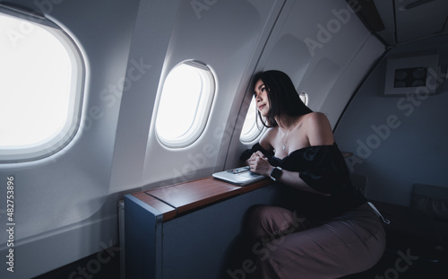 Beautiful asian woman tourist on first class passenger seat near window in airplane, travel and rest on holidays.