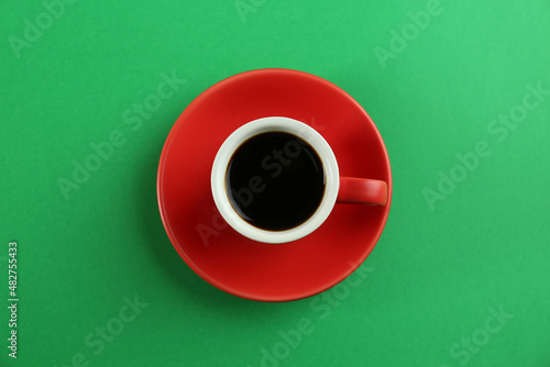 Cup of tasty coffee on green background, top view