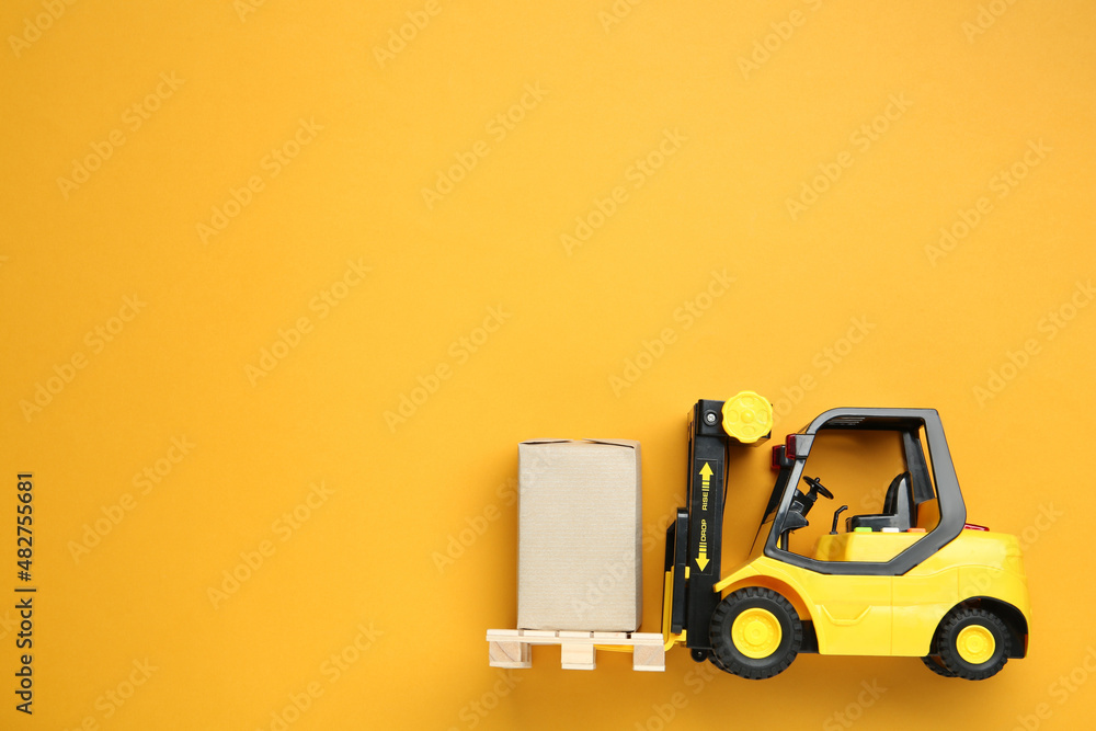 Toy forklift with wooden pallet and box on orange background, top view. Space for text Toy forklift with wooden pallet and box on orange background, top view. Space for text