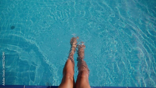 woman is swinging her legs in clear water of swimming pool, happy summer vacation