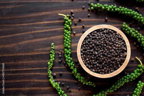 Black pepper seeds in a cup are placed on an old wooden table.