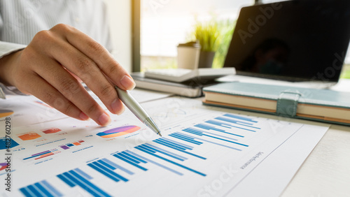 Businessman holding a profitability statistics analysis pen from a graph document in hand with a calculator and laptop on the table to plan profit growth from the past year.