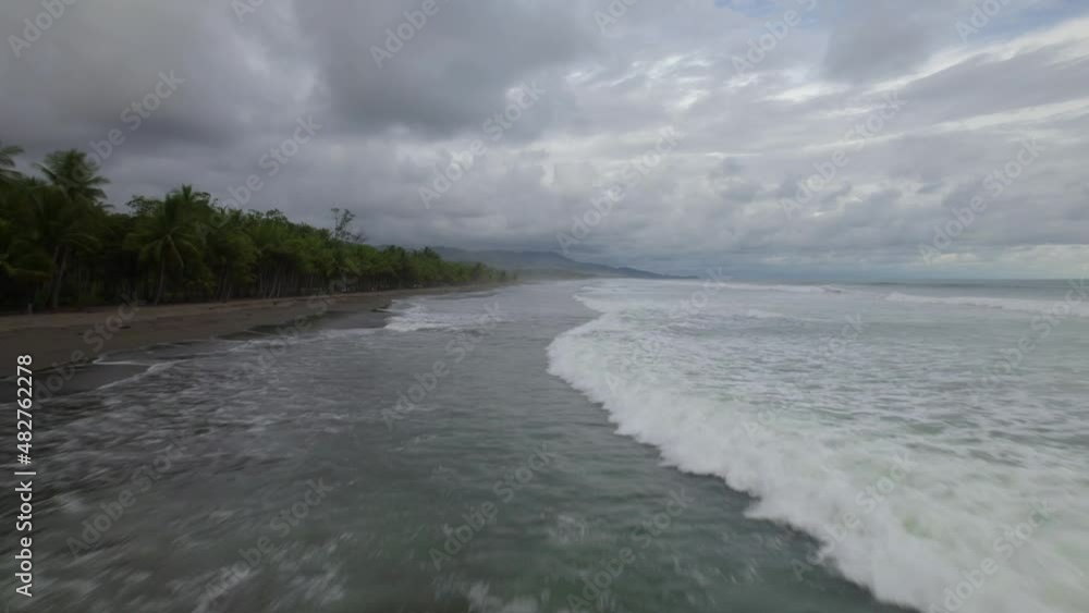 Aerial dolly in over foamy sea waves hitting the sand near dense jungle on a cloudy day in Dominicalito Beach, Costa Rica Aerial dolly in over foamy sea waves hitting the sand near dense jungle on a cloudy day in Dominicalito Beach, Costa Rica