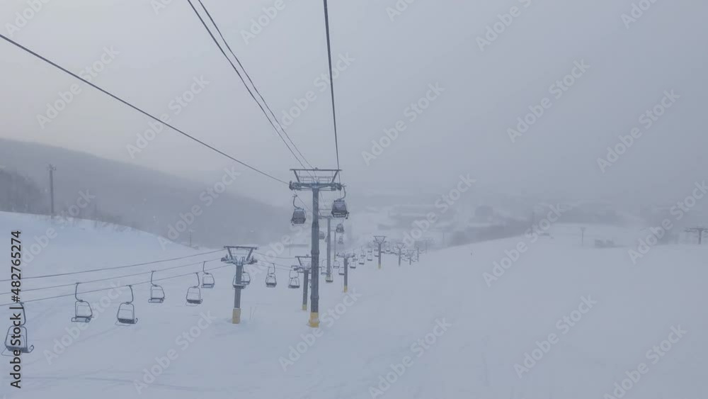 Slope in a ski resort viewed from gondola lift on snowy day (Niseko, Hokkaido, Japan)