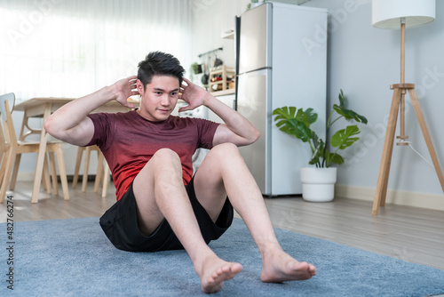 Asian handsome active young man doing sit up on floor in living room. 