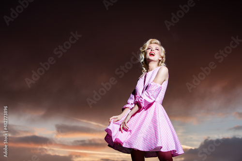 Woman in monroe dress on dramatic sky. Fashionable young model in style dress. Fashion woman in summer.