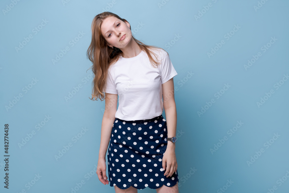 Portrait young woman casual portrait in positive look wide smile beautiful model posing in studio on blue background in casual wear in white t-shirt and polka dot skirt. Caucasian portrait woman Portrait young woman casual portrait in positive look wide smile beautiful model posing in studio on blue background in casual wear in white t-shirt and polka dot skirt. Caucasian portrait woman