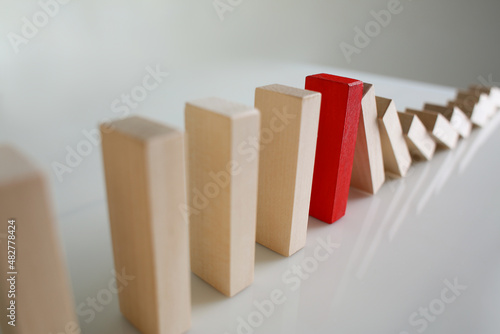 Fotografie One red wooden block stop other ones from falling like dominoes, domino effect