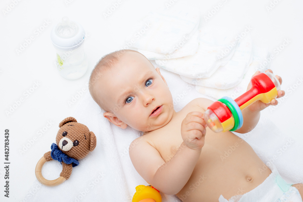 Funny little baby is wearing a diaper, playing with toys Baby after a bath or shower on a fresh towel. Changing diapers for babies and skin care. on a white background