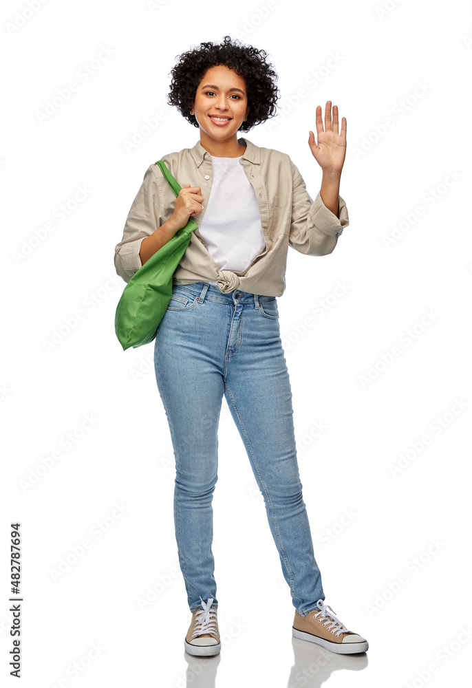 Fototapeta premium eco living, zero waste and sustainability concept - portrait of happy smiling woman with green reusable canvas bag for food shopping waving hand over white background
