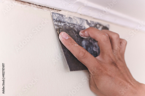 A handyman applies putty or filler to cover the gap between a wood cornice and a concrete wall with a trowel. Home improvement or renovation. photo