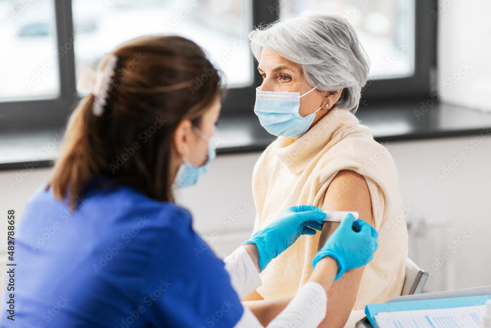 Fototapeta premium medicine, health and vaccination concept - doctor or nurse applying medical patch to vaccinated senior woman in mask at hospital