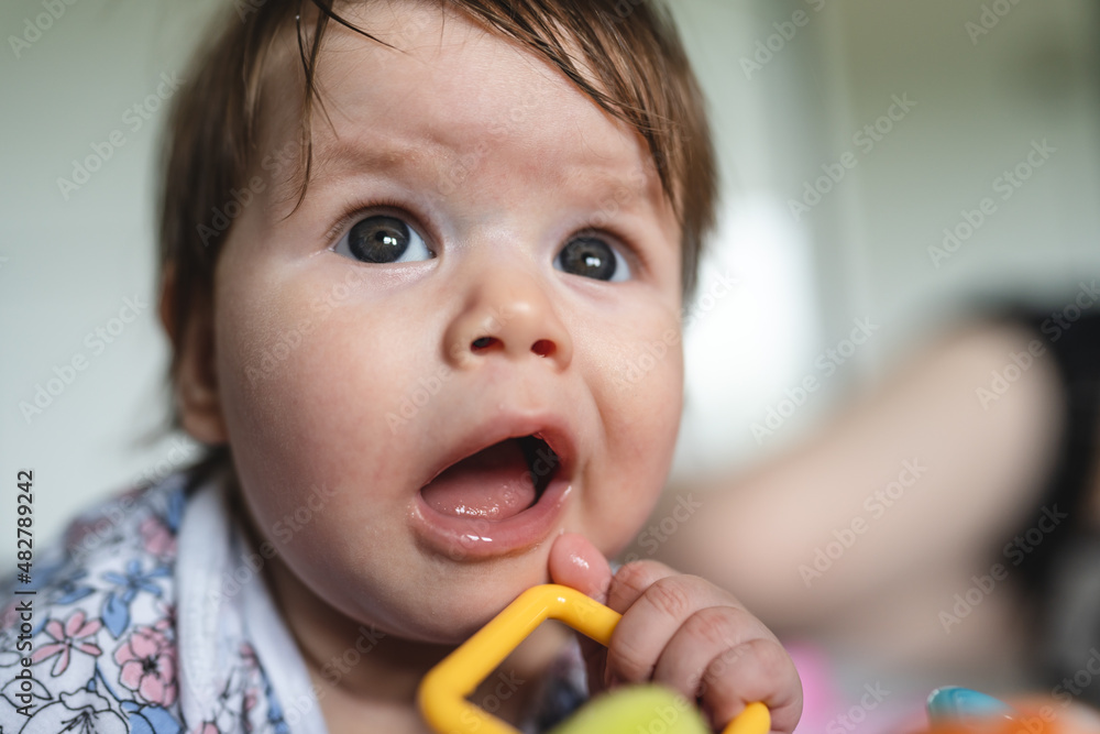 Close up on baby small caucasian girl or boy four months old lying belly down on bed at home in summer day playing with toy childhood concept Close up on baby small caucasian girl or boy four months old lying belly down on bed at home in summer day playing with toy childhood concept