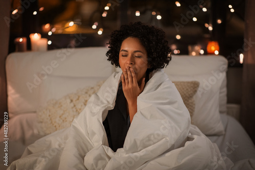 Fotografie people, bedtime and rest concept - tired sleepy woman wrapped in blanket yawning