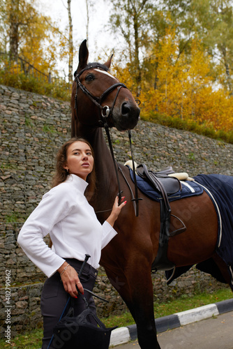 Female horseman going with her brown horse outdoor. Concept of animal care. Rural rest and leisure. Idea of green tourism. Young european woman wearing uniform