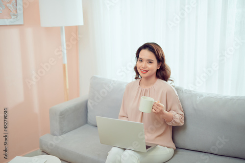 woman at remote work on a sofa near table with a laptop holding a mug