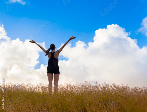 happy woman with arms up standing in grass field