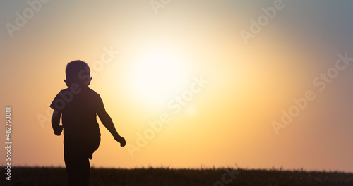 silhouette of a child little boy walking in field at sunset