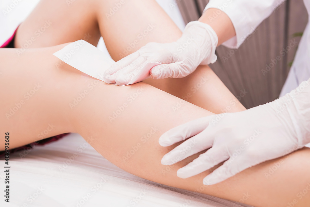 Woman with long perfect legs and smooth skin having wax stripe depilation hair removal procedure on legs in beauty salon. Woman with long perfect legs and smooth skin having wax stripe depilation hair removal procedure on legs in beauty salon.