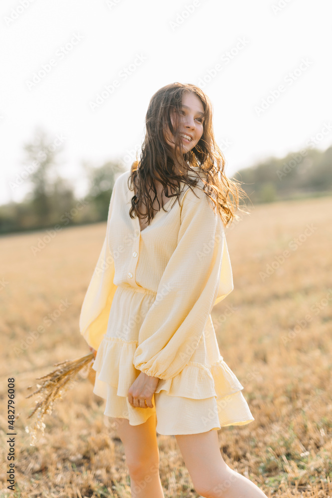 Portrait of a laughing Caucasian young brunette. girl in yellow summer dress and straw hat with a bouquet of wheat. sheared golden spike of wheat. Agricultural texture