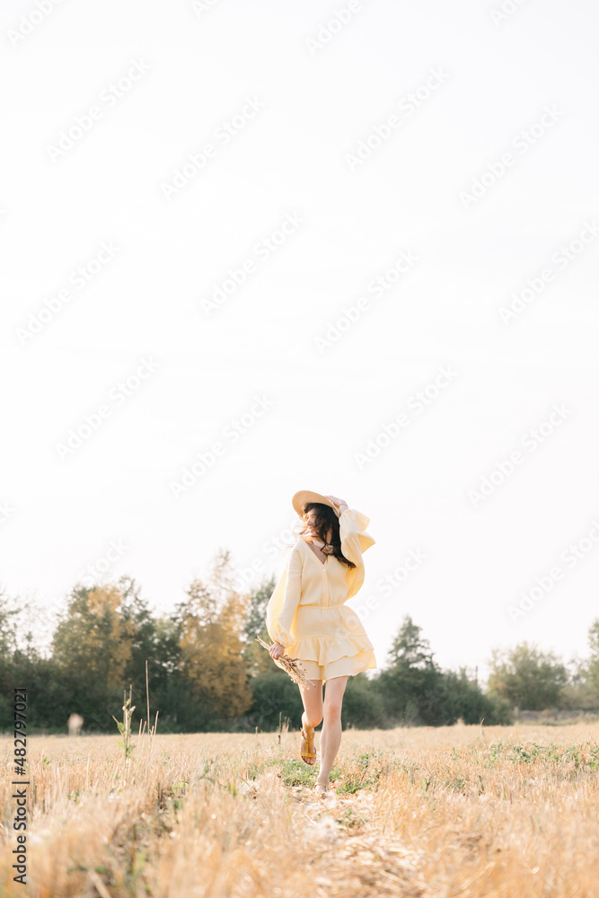Caucasian young brunette walking through a wheat field. girl in yellow summer dress and straw hat. sheared golden ears of wheat, rye. Close-up portrait of a beautiful girl with brown eyes. Caucasian young brunette walking through a wheat field. girl in yellow summer dress and straw hat. sheared golden ears of wheat, rye. Close-up portrait of a beautiful girl with brown eyes.