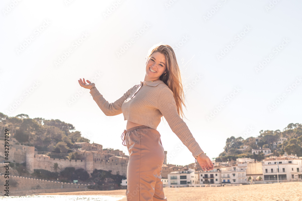 Beautiful blonde woman enjoying a sunny day in the beach walking in the sand with the arms opened, smiling looking at camera. 20-22 years old. White european woman. Beautiful blonde woman enjoying a sunny day in the beach walking in the sand with the arms opened, smiling looking at camera. 20-22 years old. White european woman.