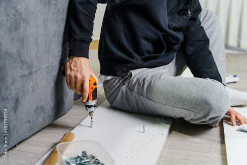 Close up on midsection of unknown caucasian man holding electric screwdriver while putting together Self assembly furniture of plywood screwing screws following instructions - DIY concept copy space