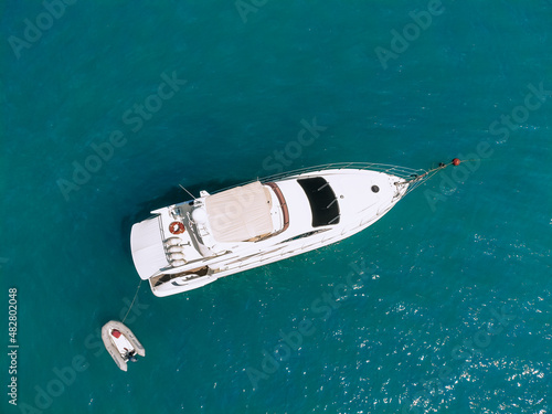 Adorable aerial top view photo of a laxury huge two-storey yach and a small boat next to it sailing across the deep blue sea
