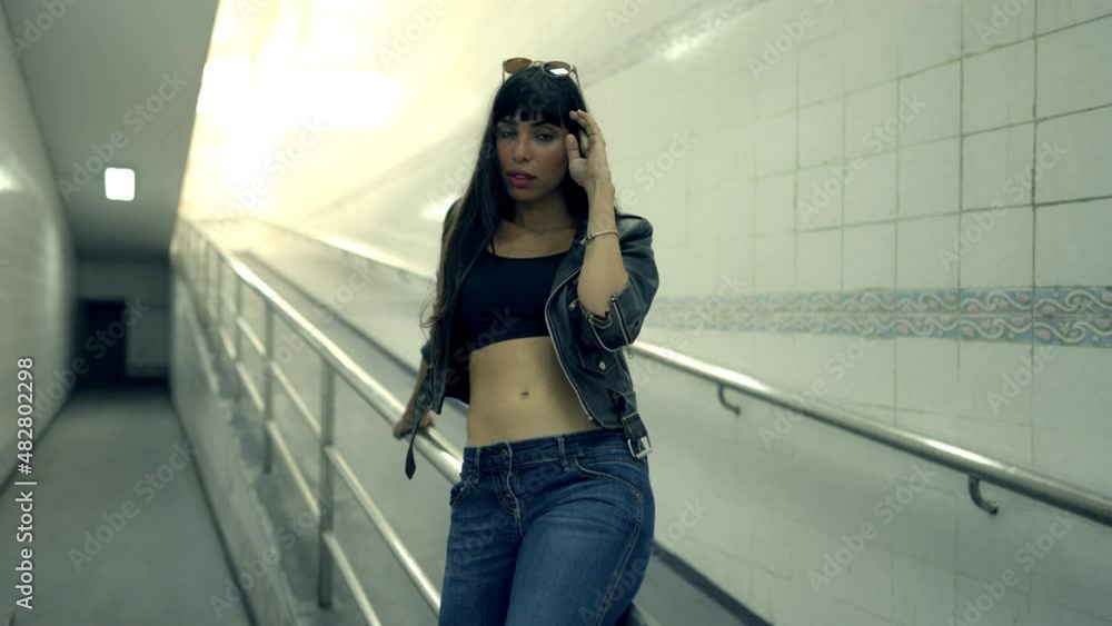 Portrait of Fashionable Hispanic woman in stylish clothing walking down cross street tunnel in the city at night. Confidence female in black leather jacket enjoy urban outdoor lifestyle and nightlife Portrait of Fashionable Hispanic woman in stylish clothing walking down cross street tunnel in the city at night. Confidence female in black leather jacket enjoy urban outdoor lifestyle and nightlife