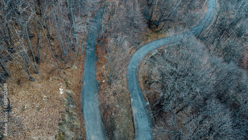 Aerial high angle view of narrow winding curvy mountain road among the trees in winter forest. Bird's eye view landscape.