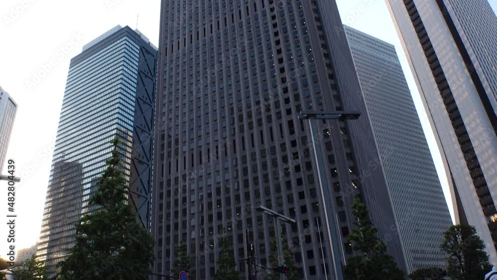 SHINJUKU, TOKYO, JAPAN - JULY 2021 : Exterior of tall office buildings in sunset time. Wide low angle time lapse shot, dusk to night. Japanese urban metropolis and business concept shot. SHINJUKU, TOKYO, JAPAN - JULY 2021 : Exterior of tall office buildings in sunset time. Wide low angle time lapse shot, dusk to night. Japanese urban metropolis and business concept shot.