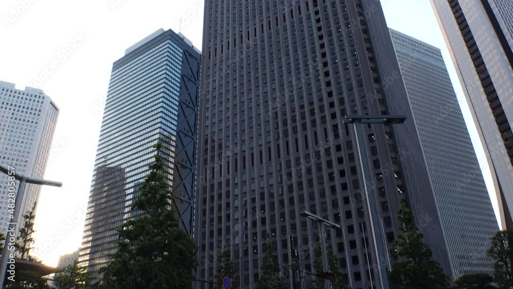 SHINJUKU, TOKYO, JAPAN - JULY 2021 : Exterior of tall office buildings in sunset time. Wide low angle time lapse shot, dusk to night. Japanese urban metropolis and business concept shot. SHINJUKU, TOKYO, JAPAN - JULY 2021 : Exterior of tall office buildings in sunset time. Wide low angle time lapse shot, dusk to night. Japanese urban metropolis and business concept shot.