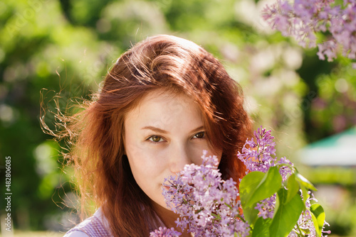 Red-haired Girl sniffing a lilac in the garden