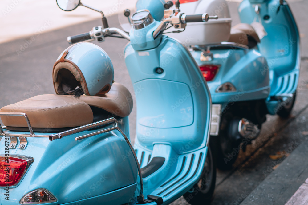 Small pretty blue motorbikes with helmets are parked near the roadway
