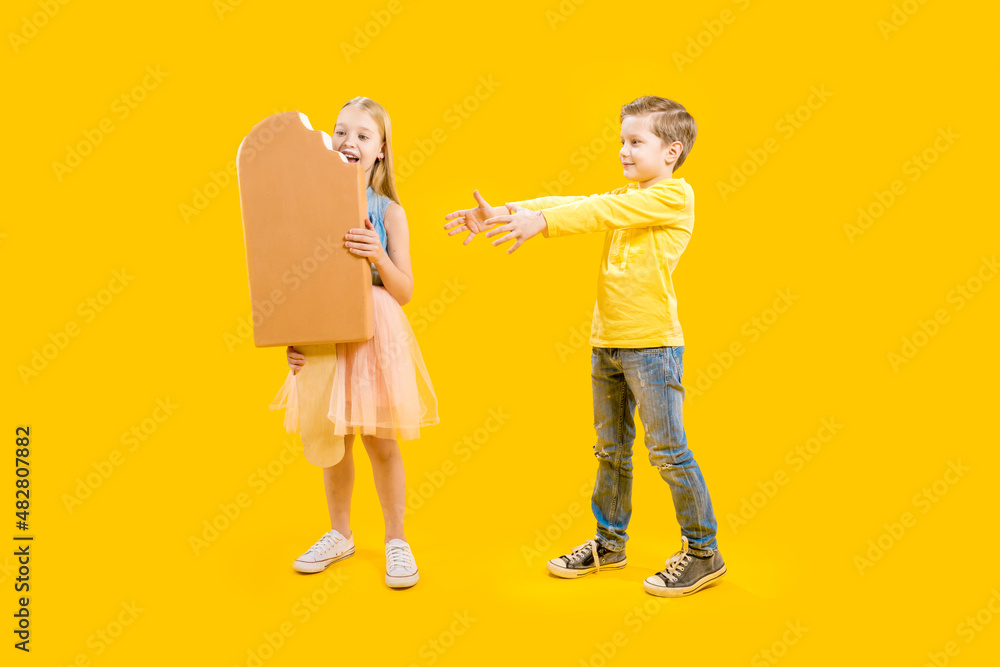 The brother is not happy that his sister does not share sweets. A huge delicious appetizing dessert. A cute girl is holding a large ice cream on a stick in her hands, a boy is standing next to her