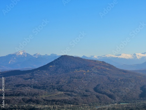 view from a high vantage point of a plateau with a rock against the background of the snowy peaks of the Caucasus Mountains in a foggy distance and the pinkish light of the winter sun