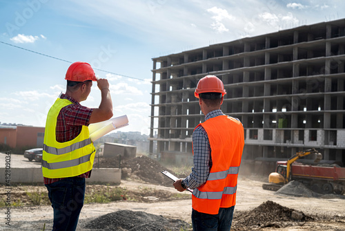 two young workers in uniforms discuss the process of building a house .