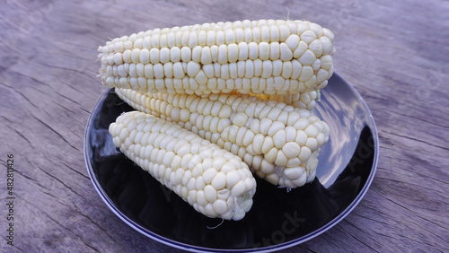 White sweetcorn is placed on a black plate on a wooden floor, healthy food, high in vitamins, nourishing the body. (2)