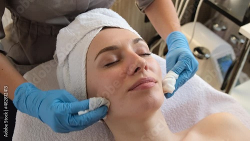 A young beautiful girl lies on the table at the beautician and receives facial cleansing procedures, makeup removal with white wipes  
